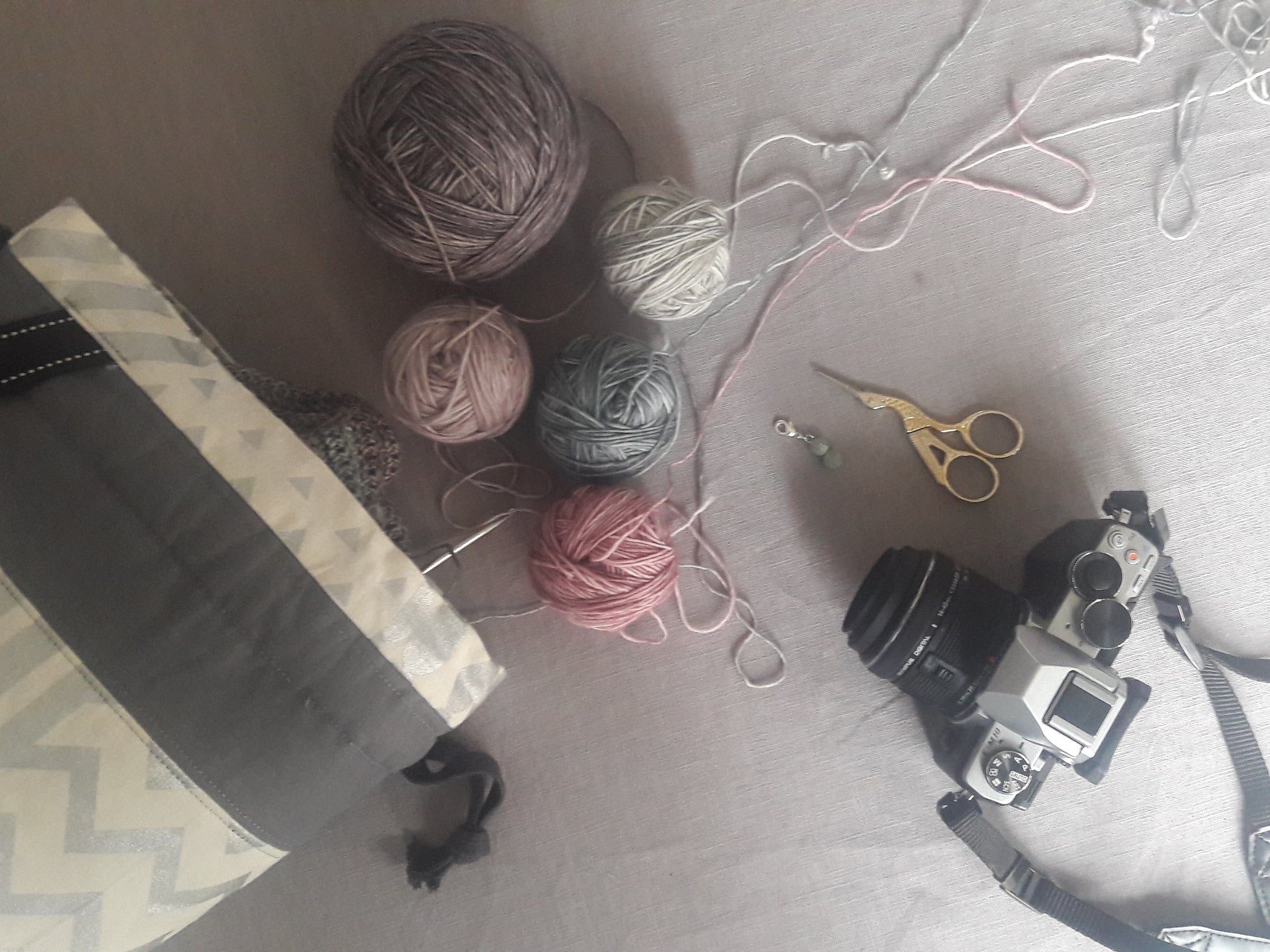 a bag of small balls of yarn spills over a grey cloth with scissors and a camera