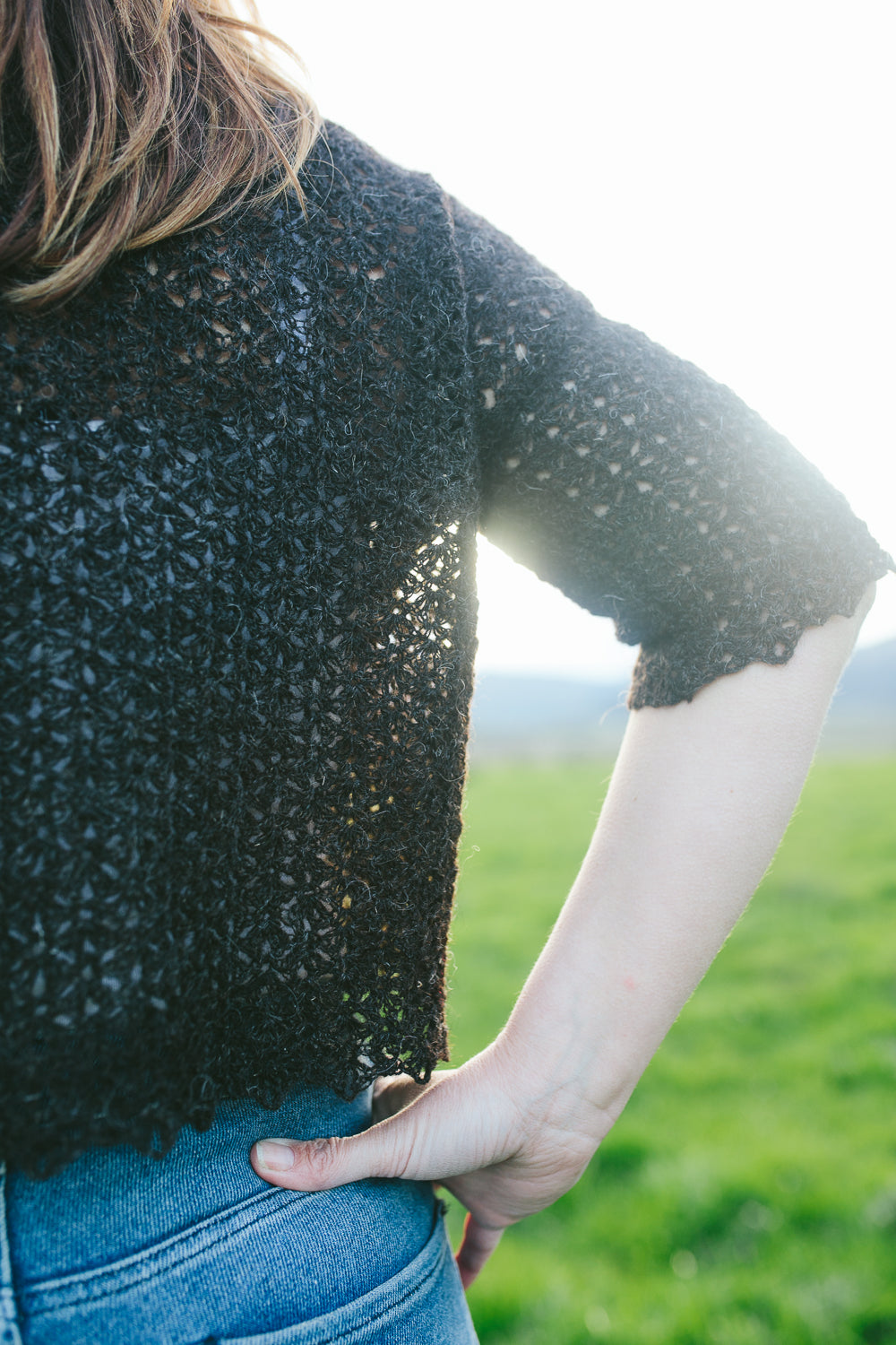 arm and side of a woman set against background of field wearing a lace crochet top (Shepherds purse tee)
