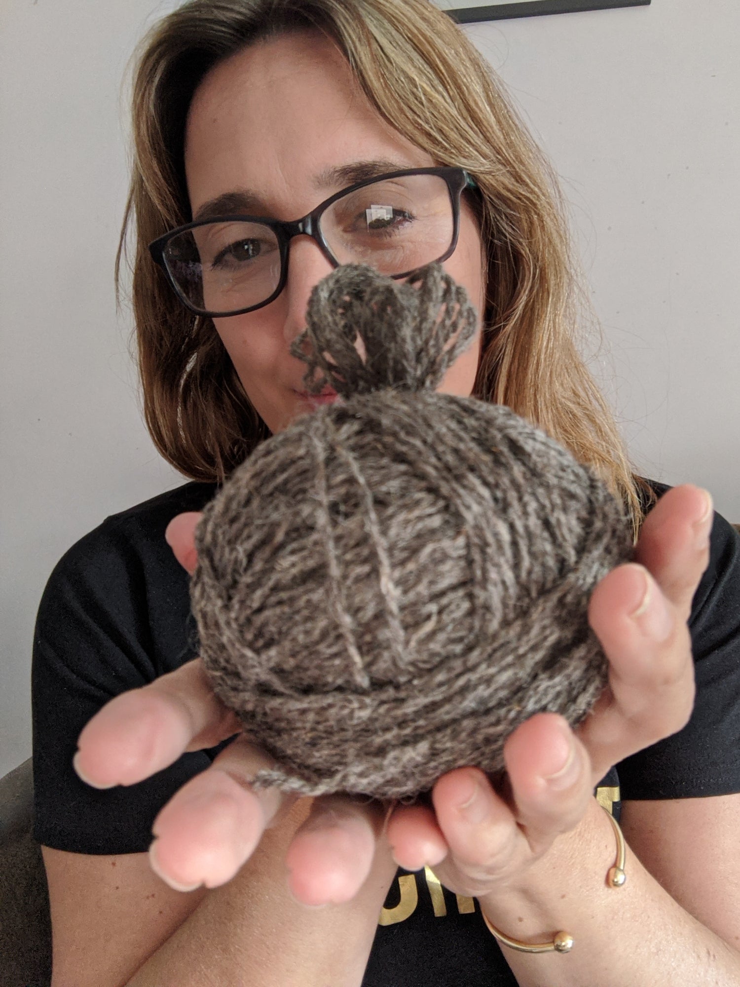 woman holds a hand wound ball of grey yarn