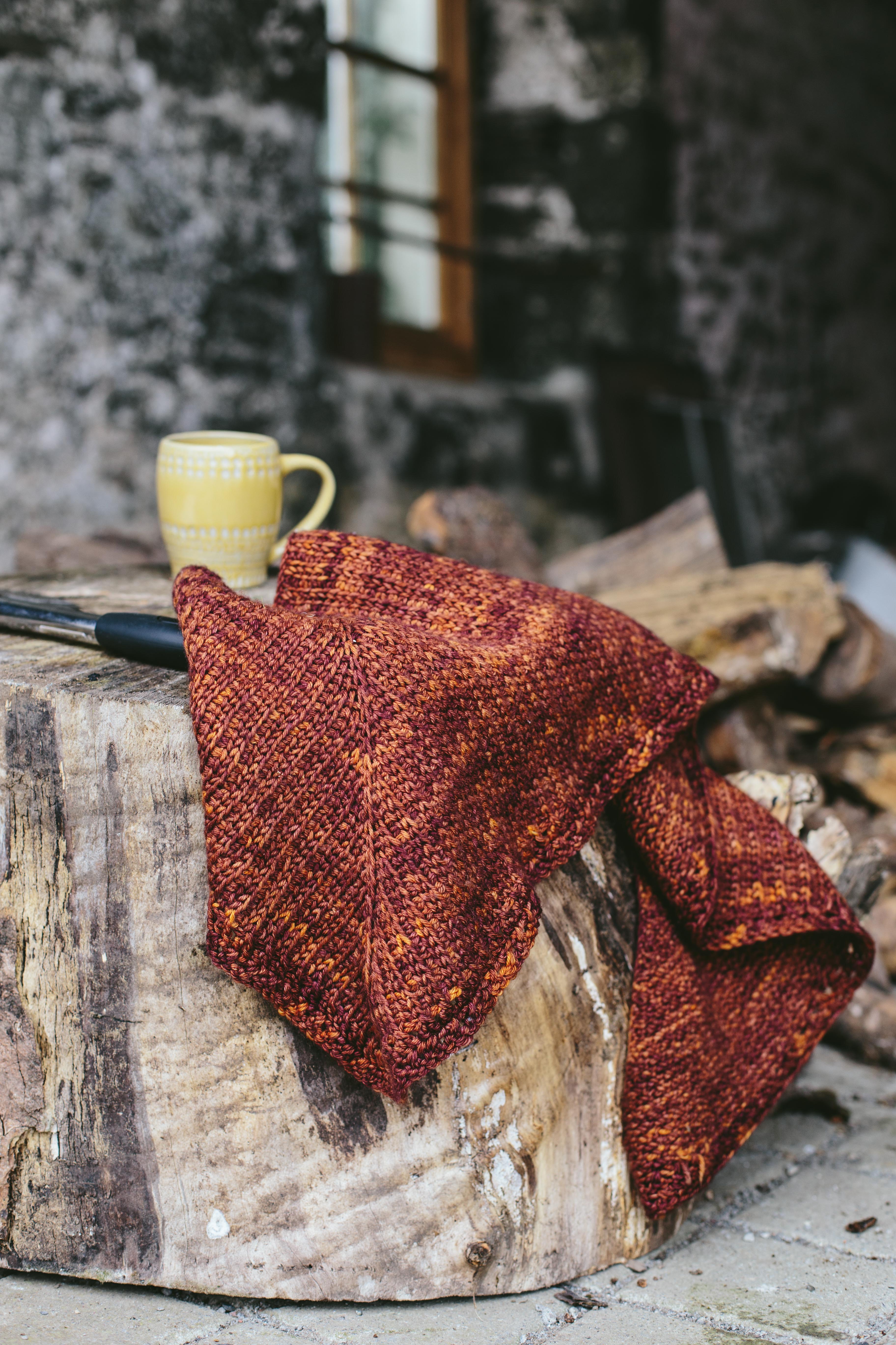 brown crochet shawl sits on a large log with a coffee mug