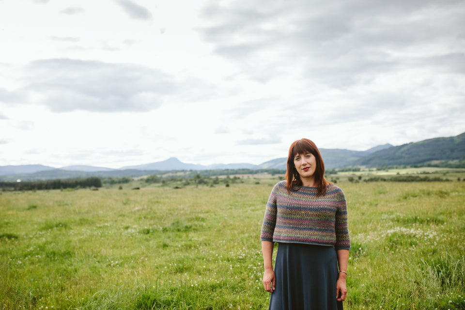 a woman wearing a crochet sweater stands in a field