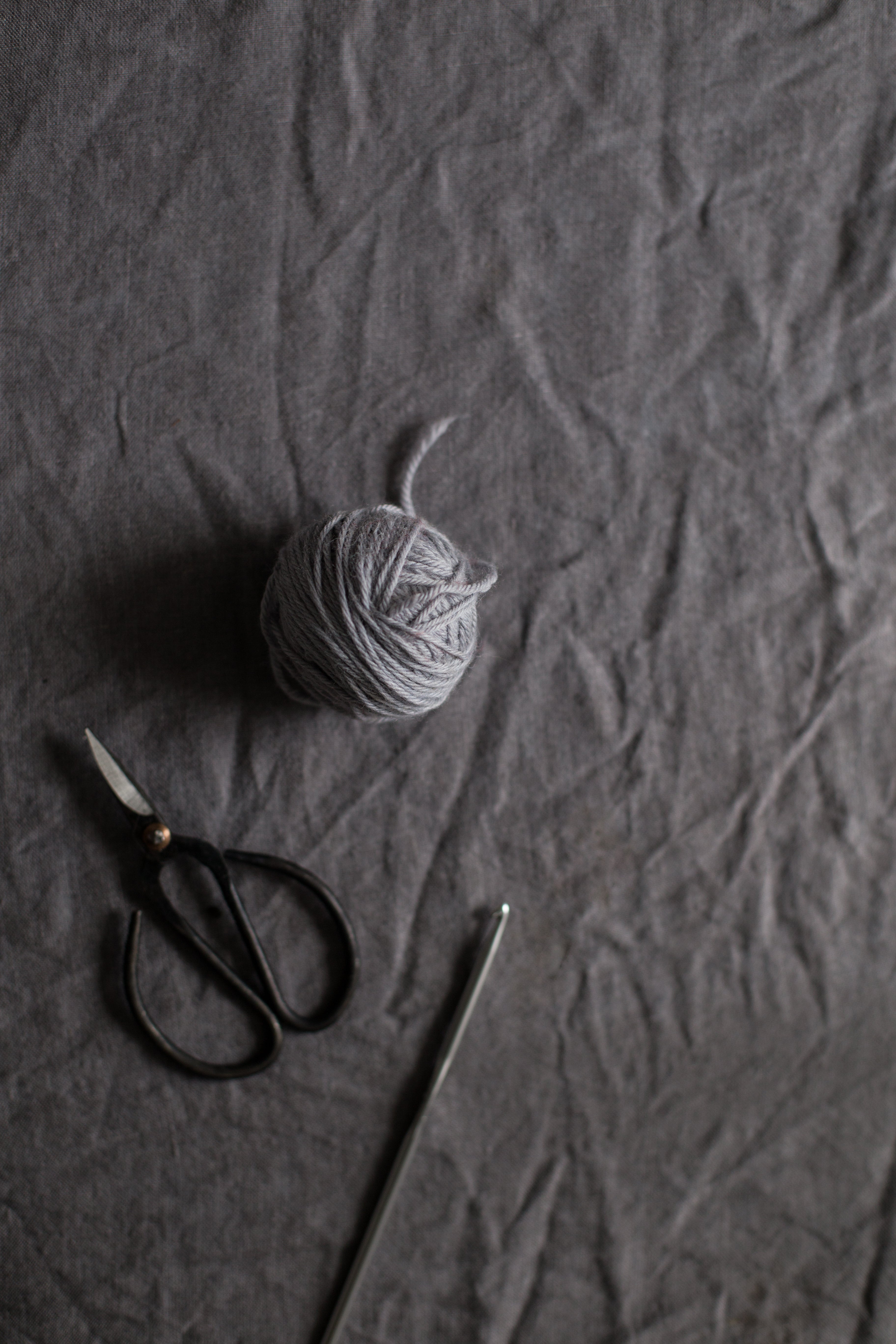 grey yarn, scrissors and hook on grey linen