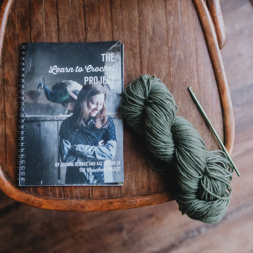 learn to crochet book, hook and skein of yarn sit on a chair
