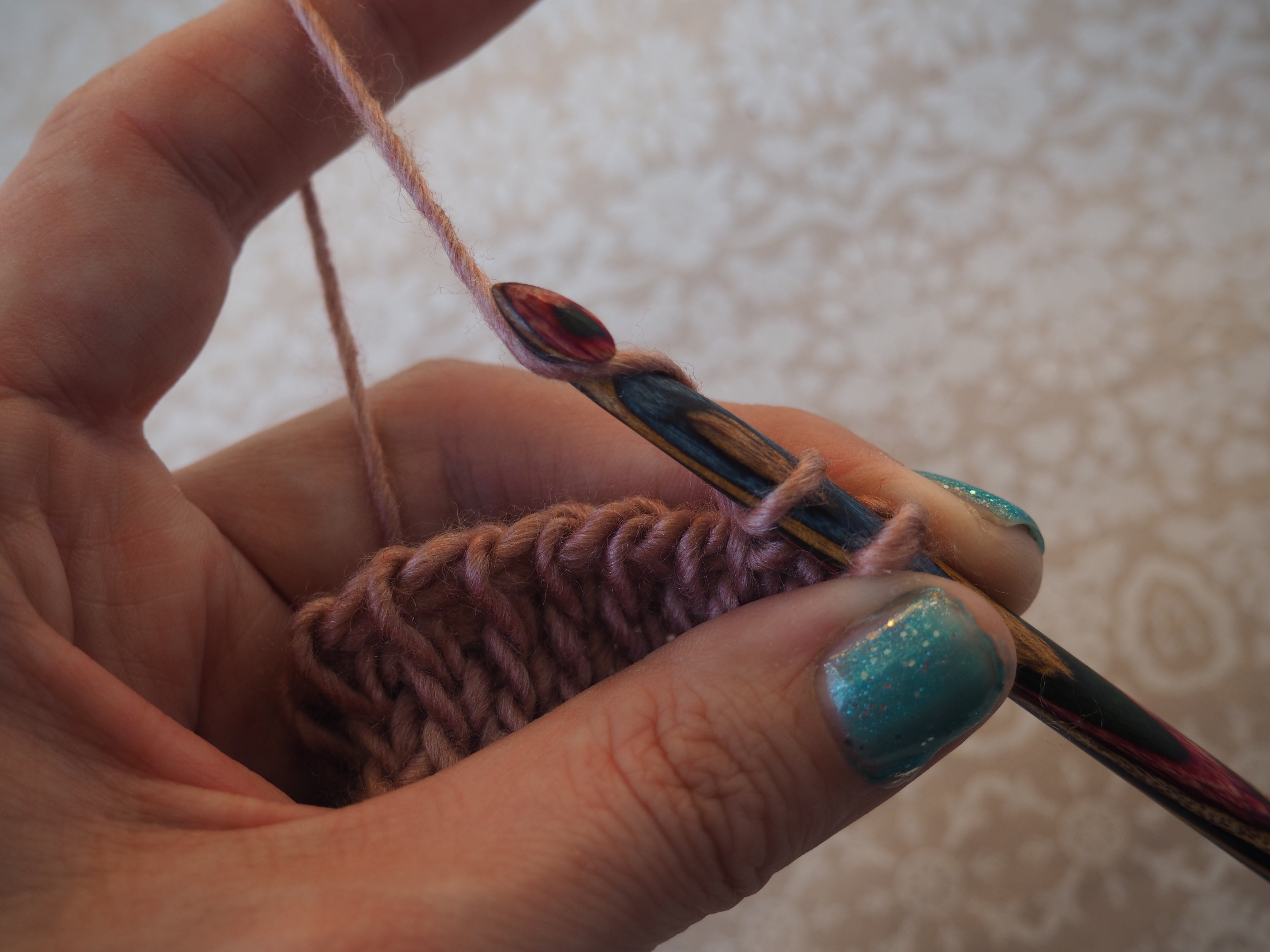 a hand holds a hook and an incomplete piece of Tunisian crochet